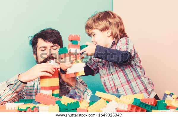 Importance of playing together. Dad and son\
have fun. Childish cheerful dad and funny son. Dad play toys with\
kid. Dad and child build plastic blocks. Happy family. Child\
development and\
upbringing.