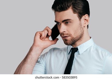 Important business talk. Serious young man in white shirt and tie talking on smart phone and looking away while standing against grey background - Shutterstock ID 583503895