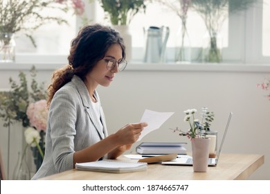 Important message. Focused attentive young woman florist designer sitting at work desk in office studio. Small business owner involved in reading paper letter from bank of credit loan terms conditions
