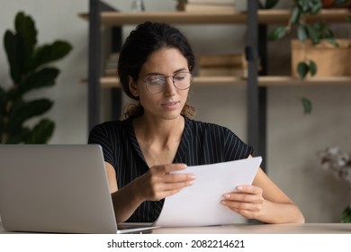 Important papers. Serious hispanic female manager in glasses engaged in office paperwork study project documentation cover letter. Young woman hr reading resume thinking on applicant cv at workplace - Shutterstock ID 2082214621
