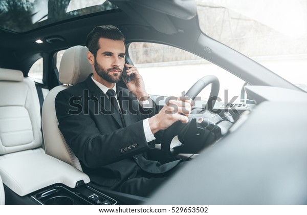 Important phone\
talk. Handsome young businessman talking on his smart phone with\
serious face while driving the\
car
