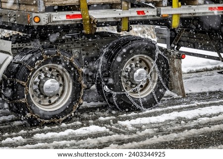 Important properly secured chains for better grip on slippery road on the wheels of the drive axles of the semi truck carrying cargo on flat bed semi trailer in winter weather during a snow storm