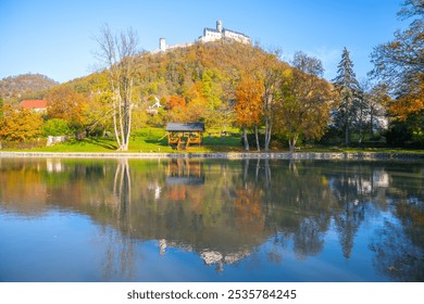 The imposing Bezdez Castle rises majestically above a tranquil lake, surrounded by vibrant autumn foliage, reflecting the historic Gothic architecture and serene landscape. - Powered by Shutterstock