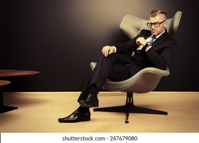 Imposing Mature Man In Elegant Suit Sitting On A Leather Chair In A Modern Luxurious Interior. Fashion. Business.