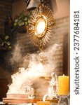 An imposing monstrance, with gleaming rays, is the abode of the Body of Christ, present in the consecrated host. The monstrance stands majestic, with Christ at the center of its golden splendor.