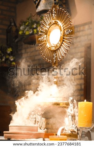 An imposing monstrance, with gleaming rays, is the abode of the Body of Christ, present in the consecrated host. The monstrance stands majestic, with Christ at the center of its golden splendor.