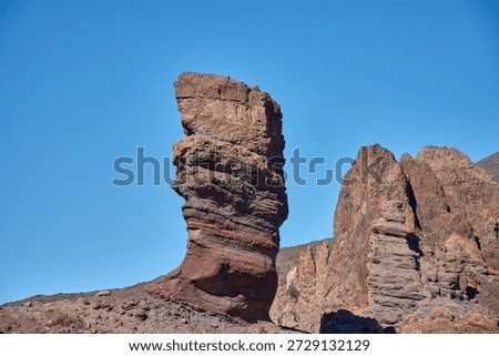 The imposing vertical structure of Roque Cinchado in the Tenerife National Park, Spain. The striking contrast between the ochre hues of the basalt rock, the white of the summit, and the intense blue of the Canary Island sky creates a visually powerful image, ideal for tourism campaigns, geography books, and travel advertising