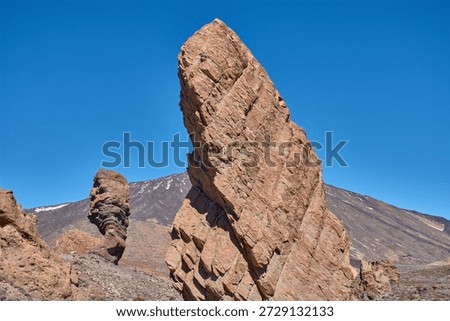 The imposing vertical structure of Roque Cinchado in the Tenerife National Park, Spain. The striking contrast between the ochre hues of the basalt rock, the white of the summit, and the intense blue of the Canary Island sky creates a visually powerful image, ideal for tourism campaigns, geography books, and travel advertising