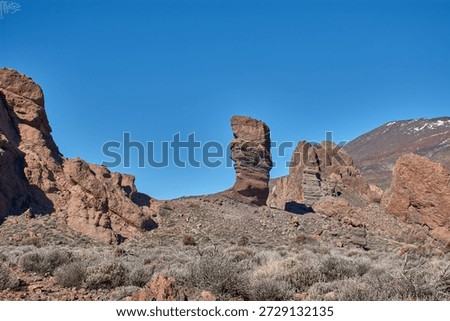 The imposing vertical structure of Roque Cinchado in the Tenerife National Park, Spain. The striking contrast between the ochre hues of the basalt rock, the white of the summit, and the intense blue of the Canary Island sky creates a visually powerful image, ideal for tourism campaigns, geography books, and travel advertising