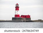 An imposing white and red lighthouse stands tall against a clear sky, its iconic tower reaching up towards the heavens