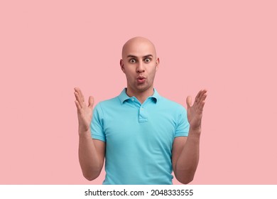 Impressed Bald Homosexual Man With Bristle Shows Big Size With Both Hands, Shapes Huge Object, Has Eyes Wide Open, Pulls Lips, Gay Friendly, Wears Blue Shirt, Stands Over Pink Background