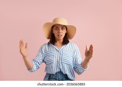 Impressed brunette makes big sign with both hands, shapes quite huge object, has eyes wide open, wears straw hat, striped shirt, jeans with belt, on pink background. Summer emotions concept