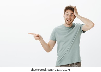 Impressed and fascinated boyfriend being excited and happy, pointing left with index finger and holding hand on head, smiling broadly, being pleased with great gift from family over gray wall - Shutterstock ID 1119701075
