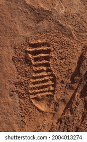 The impression of the bottom of a hiking shoe left in the fine grains of orange sand on a walking path at Page Shores Amphitheater with soft glowing afternoon light providing shadowy contrast.