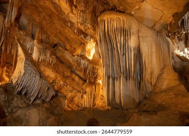Impressive cave formations featuring stalactites and stalagmites, illuminated by warm lighting, creating a majestic underground landscape