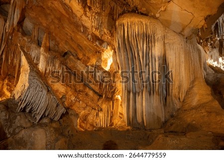 Impressive cave formations featuring stalactites and stalagmites, illuminated by warm lighting, creating a majestic underground landscape