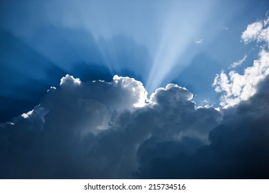 Impressive dark blue cloudscape with white cloud edges and sunbeams 