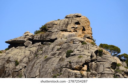 Impressive massive boulder featuring complex geological layers rising above a forested landscape.