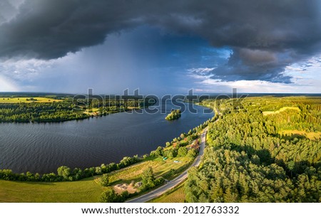 
Impressive storm clouds over the river Daugava in warm sunny day. Aerial view over colorful crop fields and pine forest.
