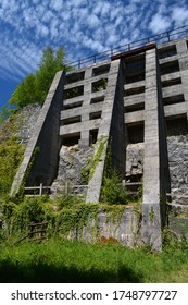 An Impressive Tall Disused Derelict Limestone Burning Kiln Constructed Of Stone And Concrete And Now Overgrown With Green Vegetation Under A Blue Summer Sky With Mottled White Clouds