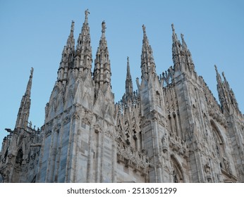 An impressive view of the intricate spires and detailed facade of Milan’s famous Duomo Cathedral. The Gothic architecture stands tall against a clear blue sky, showcasing the ornate carvings, statues - Powered by Shutterstock