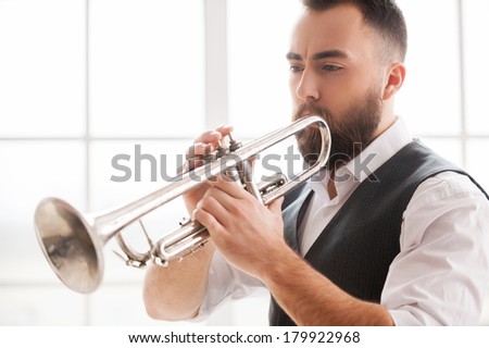 Improvising with his trumpet. Handsome bearded young men playing trumpet