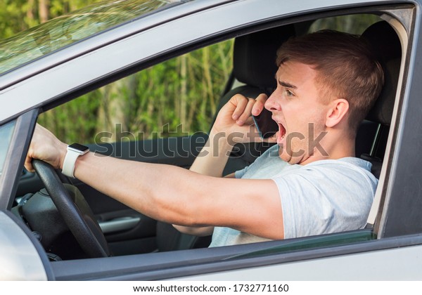 Inattentive man, frightened fearful guy,\
driver, shocked male about to have traffic accident, driving car,\
shouting screaming holding in hand, talking on cell mobile phone on\
road. Dangerous\
situation