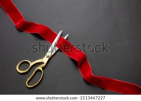 Inaugural invitation, business launch concept, Grand opening, ribbon cut, Gold scissors cutting red velvet ribbon on black background, copy space