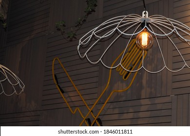 incandescent light bulb inside a metal white chandelier on the background of a fork and knife on the wall in a restaurant - Powered by Shutterstock