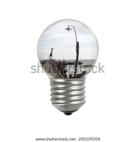 An incandescent light bulb with view of rural lamp post in a coastal village for the concept of rural electrification.