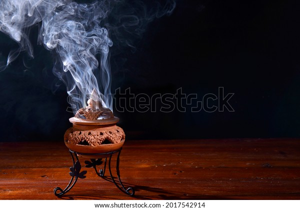incense burning in an\
incense burner on the table,with dark background.Religion\
concept.