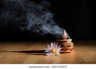 incense burning on an incense burner with beautiful flowers on the table, with a dark background. Religion concept