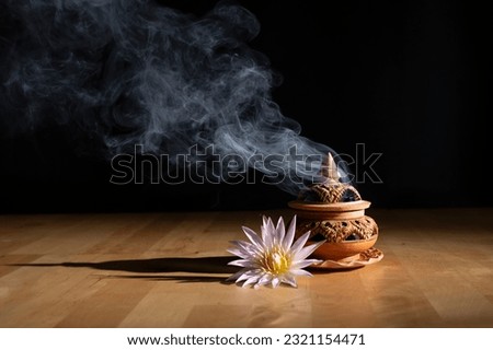 incense burning on an incense burner with beautiful flowers on the table, with a dark background. Religion concept