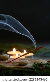 An incense stick burning and generating aromatic smoke surrounded by small candles - Shutterstock ID 2291143465