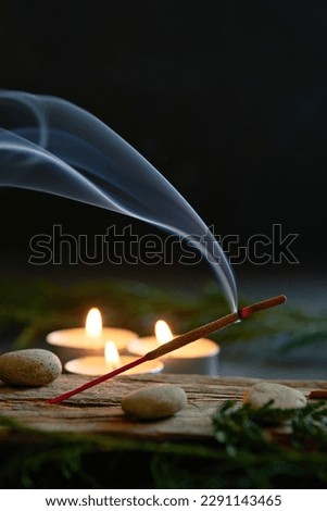 An incense stick burning and generating aromatic smoke surrounded by small candles
