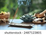 Incense stick smoldering in holder and burning candles on wooden table outdoors