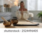 Incense stick smoldering in holder and tibetan singing bowls on wooden table indoors, selective focus