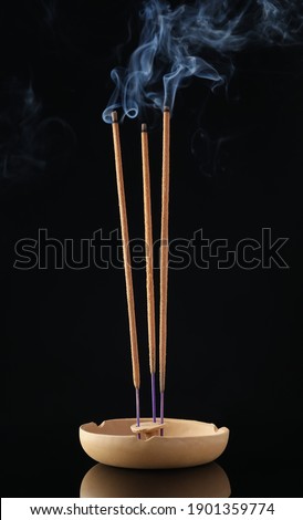 Incense sticks smoldering in holder on black background