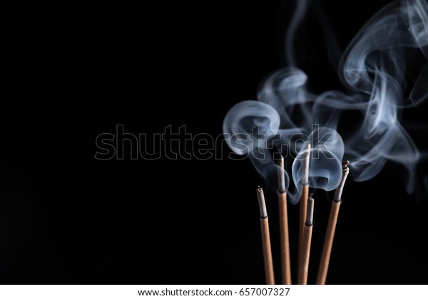 Incense sticks and incense stick smoke on black\
backgrond with white\
backlit