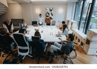 Inclusive business meeting with a diverse team engaged in discussion. A member in a wheelchair actively participating adds to the dynamic. - Powered by Shutterstock