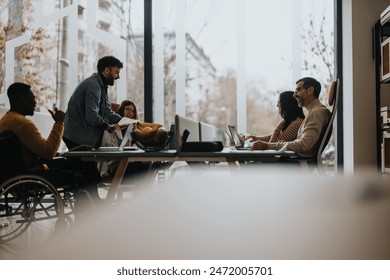 An inclusive modern office environment with professionals collaboratively working. A man in a wheelchair actively participates in a business meeting. - Powered by Shutterstock