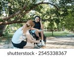 Inclusive Outdoor Activity: Young Woman Assisting a Smiling Man in a Wheelchair Enjoying a Sunny Day in the Park