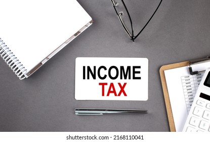 INCOME TAX Text written on card with notebook and clipboard, grey background