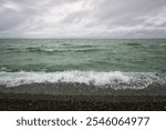 An incoming wave on the Black Sea and a pebble beach on the Sochi coast on a summer day with clouds, Sochi, Krasnodar Territory, Russia