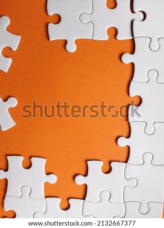 Incomplete disassemble white jigsaw puzzle, missing puzzle pieces showing orange background 