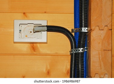 An Incomplete Internal Electrical Power Box In A Wooden House, For Use As A Switch Or Plug Socket, With A Black Plastic Covering Tube For Wiring Protection. Tubing Going Up Protects Solar Heater Pipes