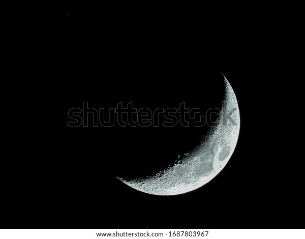 the increasing sickle-shaped\
quarter moon with its moon craters stands in the black night\
sky