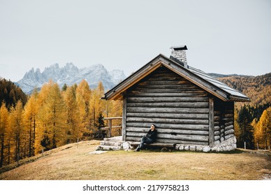 Incredible autumn view at Valfreda valley in Italian Dolomite Alps. Wooden cabin, yellow grass, orange larches forest and snowy mountains peaks on background. Dolomites, Italy. Landscape photography