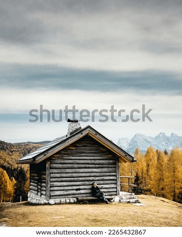 Incredible autumn view at Valfreda valley in Italian Dolomite Alps. Wooden cabin, yellow grass, orange larches forest and snowy mountains peaks on background. Dolomites, Italy. Landscape photography