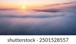 Incredible dawn, the sun rises above the low fluffy clouds that enveloped the earth. Concept of peace and relaxation, idyllic vibe. Aerial photography. Photo wallpaper. Discovery the beauty of earth.